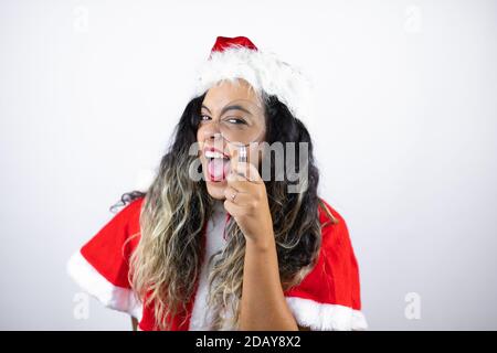 Junge schöne Frau trägt ein Weihnachtsmann Kostüm über weiß Hintergrund überrascht Blick durch eine Lupe Stockfoto