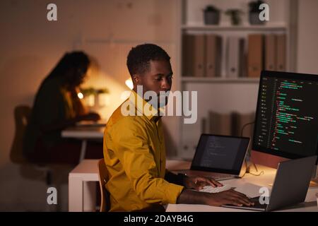 Portrait von afroamerikanischen IT-Entwickler schreiben Code auf mehreren Computer-Bildschirme während der Arbeit spät im Büro, Copy Space Stockfoto