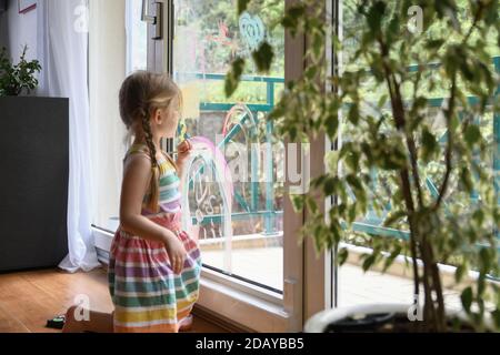 Mädchen zeichnet einen Regenbogen und Blumen auf das Fenster Stockfoto