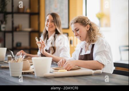 Töpferinnen während des Arbeitsprozesses in der Tonwerkstatt. Frau Meister bereiten Keramik-und Ton-Produkte an großen Holztisch Stockfoto