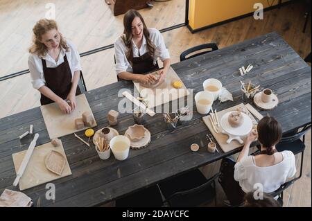 Töpferinnen während des Arbeitsprozesses in der Tonwerkstatt. Frau Meister bereiten Keramik-und Ton-Produkte an großen Holztisch Stockfoto