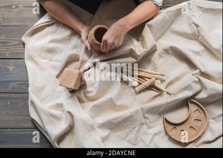 Eine junge Töpferin, die Topf in ihrem eigenen Arbeitsplatz macht. In einem geräumigen Studio stehend und mit ihren Händen die Form des zukünftigen Produkts erschaffen. Stockfoto