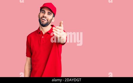 Junge gut aussehende Mann mit Bart tragen Lieferung uniform lächelnd freundlich bietet Handschlag als Begrüßung und Begrüßung. Erfolgreiches Geschäft. Stockfoto