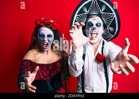 Schönes Paar trägt Tag der Toten Kostüm gestikuliert als Zombie über isolierten roten Hintergrund. Stockfoto