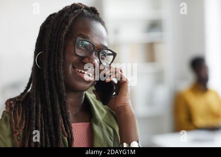Nahaufnahme Porträt der stilvollen jungen afrikanischen Frau sprechen mit dem Smartphone im Büro und lächeln, Kopierraum Stockfoto