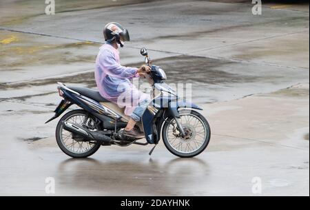 SAMUT PRAKAN, THAILAND, JULI 24 2020, EIN Mann im Regenmantel fährt auf nasser Straße mit dem Motorrad. Stockfoto