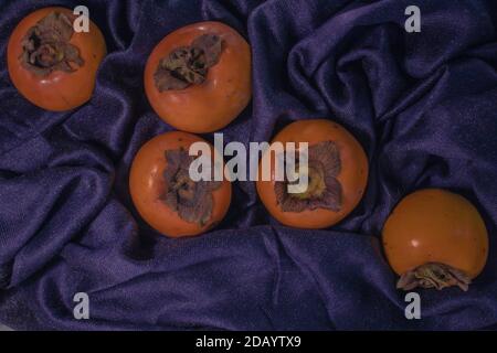 Verstreute orange frische Kaki-Früchte auf einem dunkelblauen zerknittert Stoff Stockfoto