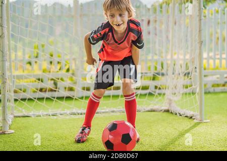 Kleine niedliche Junge in roten Fußball-Uniform Fußball spielen, Fußball auf dem Feld, im Freien. Aktives Kind macht Sport mit Kindern oder Vater, lächelnd glücklich Stockfoto