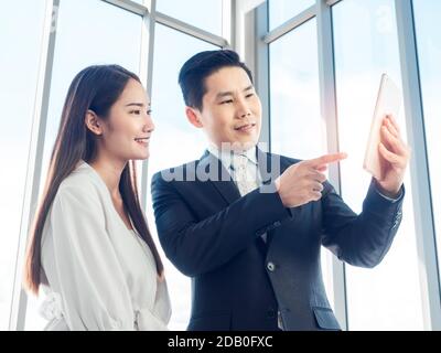 Asiatische Geschäftsmann in Anzug und junge Frau macht Videoanruf mit digitalen Tablet auf Glasfenster Hintergrund. Videokonferenz oder Online-Seminar, commun Stockfoto