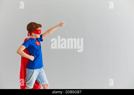 Kleiner lächelnder Junge in einem Superhelden Kostüm mit rotem Umhang und Brille ist bereit für Abenteuer. Stockfoto