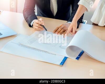 Frau Hand zeigen Blaupause auf Holzschreibtisch im Büro mit Ingenieur im Anzug mit Stift zeigen, auch. Geschäftsmann und Frau arbeiten zusammen, investtig Stockfoto
