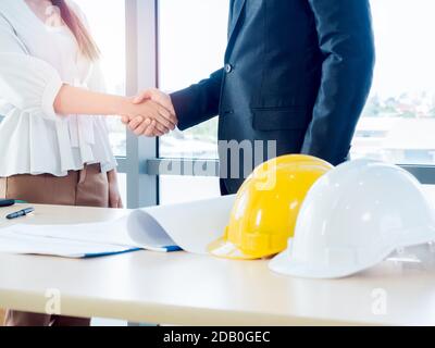 Handshake des Collaboration-Konzepts. Geschäftsmann im Anzug, Ingenieur oder Architekt und Frau schüttelt die Hände auf Blaupause und gelb und weiß Sicherheit har Stockfoto
