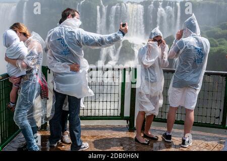 Besucher tragen Plastikwasserschutzmäntel vom Spray auf der Aussichtsplattform auf der brasilianischen Seite der Iguazu Wasserfälle in Brasilien. Stockfoto