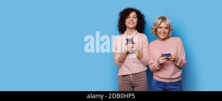 Charmante blonde Dame mit ihrem lockigen behaarten Freund chatten Auf einer blauen Studiowand nahe dem freien Raum lächelnd an Kamera Stockfoto