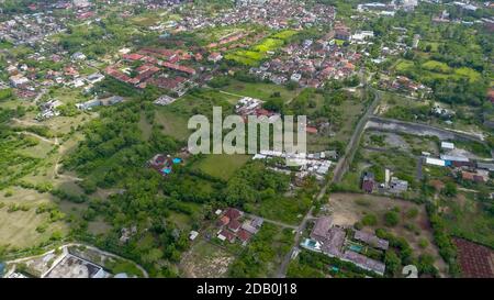 Viele Villen mit braun-orangen Schindeldächern zwischen tropischen Bäumen am Himmel Hintergrund in Ubud auf Bali. Die Sonne scheint auf sie. Luftaufnahme Stockfoto