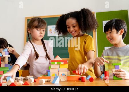 Gruppe von multiethnischen Schulfreunden mit Spielzeugblöcken im Klassenzimmer, Bildung, Lernen, Teamarbeit. Kinder spielen mit Holzblöcken im Klassenzimmer Stockfoto