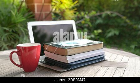 Gesichtsmaske auf gestapelten Büchern und offenen Computer-Laptop mit roter Tasse. Studie zu Hause während des Pandemiekonzepts. Stockfoto