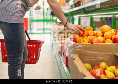 Porträt einer niedlichen jungen Frau mit einem Korb in den Händen, die Äpfel im Supermarkt wählt. Nahaufnahme. Stockfoto