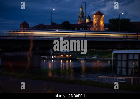 Zug fährt über die Brücke mit dem Wawel Schloss im Hintergrund in Krakau, Polen an einem Sommerabend neben der Weichsel. Stockfoto