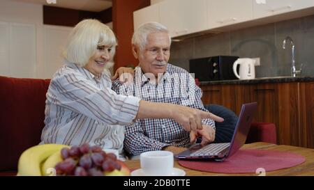 Ältere alte Großeltern paar reden und mit digitalen Laptop-Computer zu Hause. Online-Shopping. Ältere Großvater und Großmutter genießen Zeit während Coronavirus covid-19 Lockdown Stockfoto