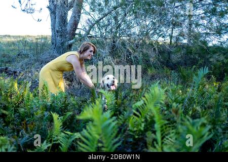 Blonde Dame liebt ihren Golden Retriever Hund im Wald Stockfoto