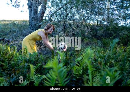 Blonde Dame liebt ihren Golden Retriever Hund im Wald Stockfoto