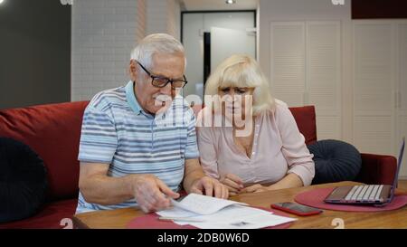 Gestresste Senior-Paar diskutieren unbezahlte Bankschulden halten Rechnungen, tun Papierkram, Planung Haushalt, Finanzen berechnen Hypothekenzahlungen zu Hause zu diskutieren. Besorgte ältere Großmutter wirft Papierrechnungen Stockfoto