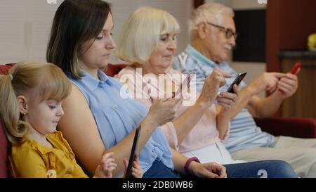 Süchtig nach Gadgets Familie mit Handy, Tablet, Laptop ignorieren einander zu Hause. Ältere Paar, Frau und Kind Mädchen Kind in Chat in sozialen Netzwerken beteiligt, Internet-Obsession Konzept Stockfoto
