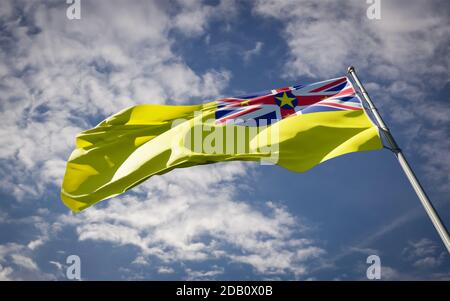 Schöne Nationalflagge von Niue flattert am Himmel Hintergrund. Nahaufnahme mit Niue-Flag-3D-Grafik mit niedrigem Winkel. Stockfoto
