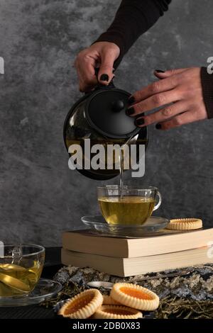 Frau Hände gießt Tee aus einer Teekanne Stockfoto