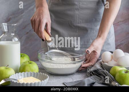 Frau sieben Mehl durch Sieb, die Zubereitung von hausgemachten süßen Kuchen mit reifen Äpfeln Stockfoto