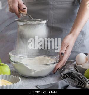 Frau sieben Mehl durch Sieb, die Zubereitung von hausgemachten süßen Kuchen mit reifen Äpfeln Stockfoto