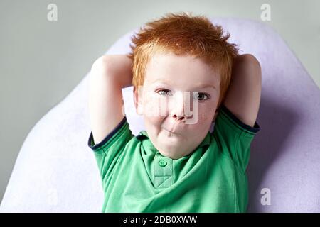 Nahaufnahme Porträt eines niedlichen rothaarigen Sommersprossen kleinen Jungen Im grünen T-Shirt warten auf Arzt in der Arztpraxis Stockfoto