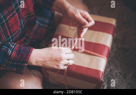 Frau Verpackung Weihnachtsgeschenke sitzen auf dem Boden in einem roten karierten Hemd. Rustikale Weihnachtsstimmung. Stockfoto