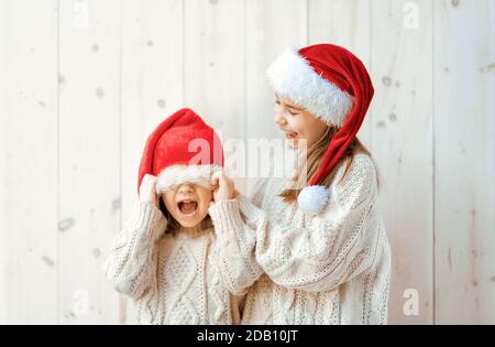 Glückliche kleine Mädchen in Santa's Hüte auf weißem Holzhintergrund. Weihnachtszeit. Stockfoto