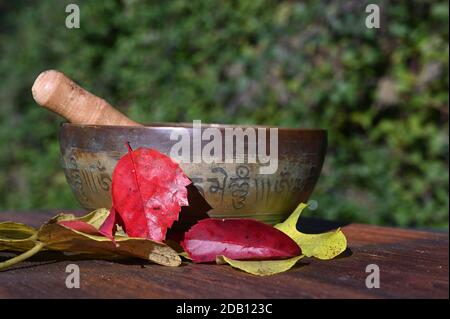 Eine singende Schüssel mit Herbstblättern auf einem Holzbrett Stockfoto