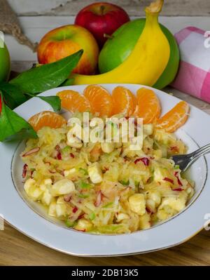 Gesunder Obstsalat mit geraspelten roten und grünen Äpfeln, Bananen und Orangen auf einem Teller auf rustikalem Küchentisch Stockfoto