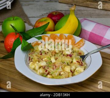 Gesunder Obstsalat mit geraspelten roten und grünen Äpfeln, Bananen und Orangen auf einem Teller auf rustikalem Küchentisch Stockfoto