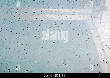 Regentropfen laufen auf einem Glasfenster, heller Hintergrund Stockfoto