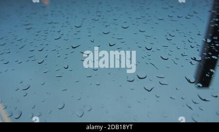 Regentropfen laufen auf einem Glasfenster, blauer Hintergrund Stockfoto