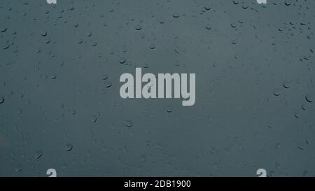 Regentropfen laufen auf einem Glasfenster, dunkelblauer Hintergrund Stockfoto