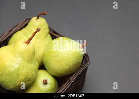 Grüne Birnen in einem Weidenkorb auf dunklem Hintergrund Stockfoto