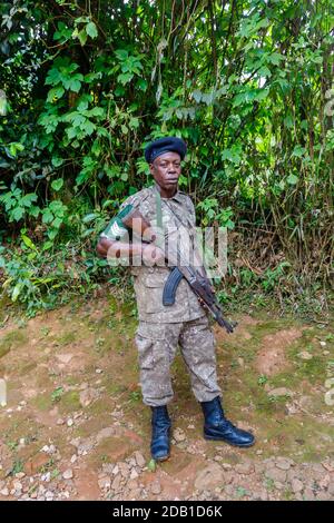 Lokaler afrikanischer mürrischer bewaffneter Wachmann, der mit einem Sturmgewehr vor dem Engagi Lodge Hotel im Bwindi Impenetrable Forest, Uganda, steht Stockfoto