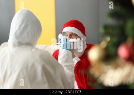 Arzt im Schutzanzug misst die Temperatur des Menschen in santa claus-Anzug Stockfoto