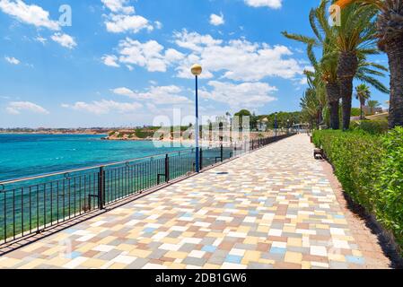 Malerische Strandpromenade von Punta Prima. Leerer eingezäunter Fußgängerweg und türkisfarbenes Mittelmeer. Costa Blanca, Spanien. Sommerurlaub, Stockfoto