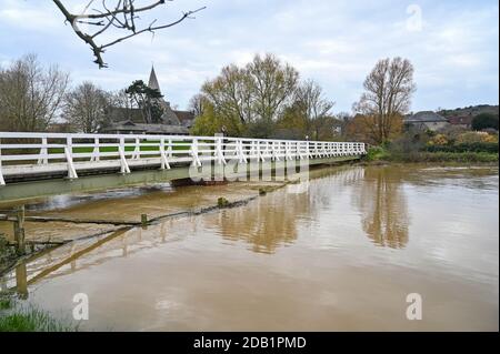 Alfriston Sussex UK 16. November 2020 - Wanderer überqueren eine Brücke über hohe Wasserstände am Fluss Cuckmere in Alfriston bei Seaford in East Sussex nach den jüngsten starken Regenfällen und ungewöhnlich hohen Gezeiten. Hochwasserwarnungen wurden in ganz Großbritannien nach dem jüngsten nassen Wetter ausgegeben, aber kältere Bedingungen werden für später in der Woche prognostiziert : Credit Simon Dack / Alamy Live News Stockfoto