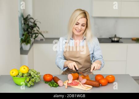 Lächelnde Frau bereitet etwas zu essen, Frau schneidet Wurst Stockfoto