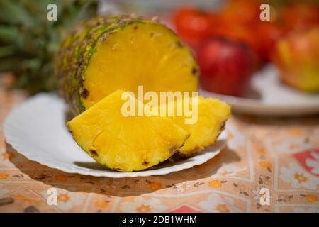 Ananasfrucht auf weißem Teller und rote Äpfel im Hintergrund. Stockfoto