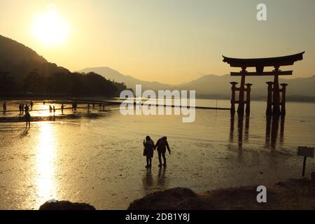 Japan Vermilion Torii Itsukushima-Jinja auf Miyajima. Sonnenuntergangsszene mit Silhouette von Paaren. Ruhige, spirituell entspannende, romantische Peace Island. Stockfoto