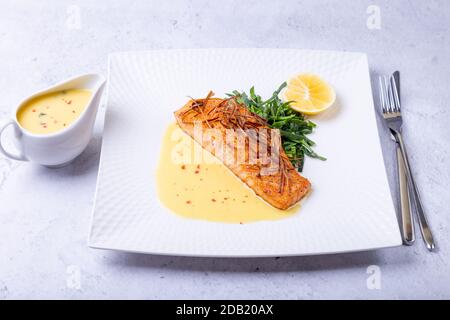 Lachs mit Beurre Blanc Sauce, Spinat und Zitrone. Garniert mit Lauch. Traditionelles französisches Gericht. Nahaufnahme. Stockfoto